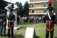 In primo piano uno dei due lati del cippo dedicatorio fra i carabinieri in uniforme speciale di rappresentanza. 
Sul fondo le a